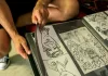 Student sztuki układa rysunki komiksowe w foliowym portfolio na kolanach.