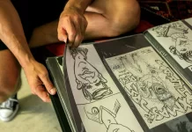 Jak budować portfolio podczas studiów artystycznych Student sztuki układa rysunki komiksowe w foliowym portfolio na kolanach.