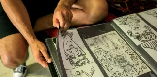 Student sztuki układa rysunki komiksowe w foliowym portfolio na kolanach.