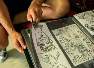 Student sztuki układa rysunki komiksowe w foliowym portfolio na kolanach.