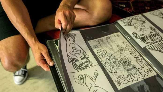 Student sztuki układa rysunki komiksowe w foliowym portfolio na kolanach.